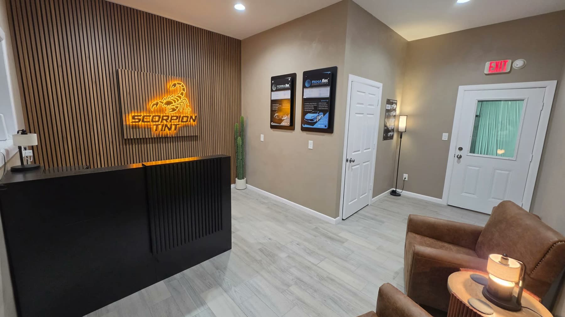 The Scorpion Tint waiting room — backlit logo on a wood slat wall, window film sample boards, and leather seating
